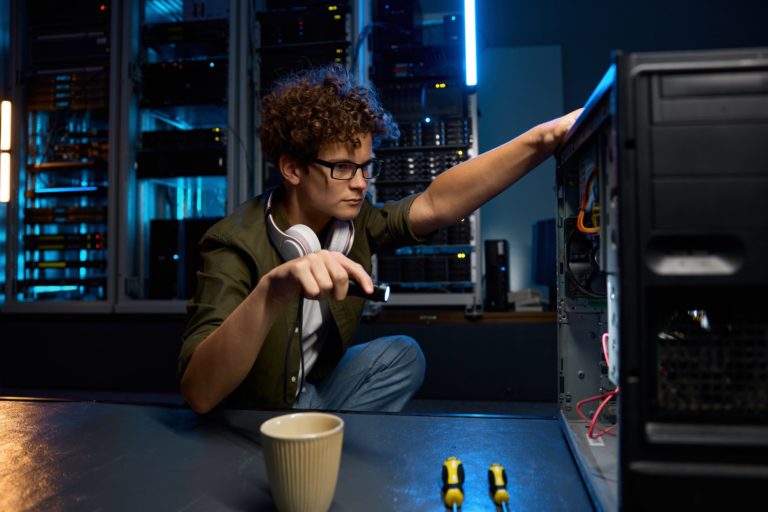 Young IT technician using flashlight to find problem with computer in modern data center